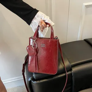 Red patent leather mini crossbody bag for women, stylish tote purse with heart charm pendant.