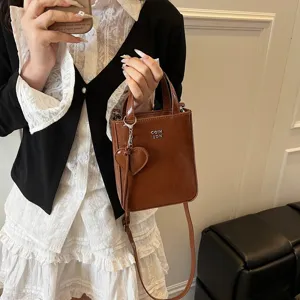 Brown patent leather crossbody bag with top handle and cute heart charm for women.