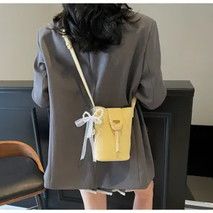 Mini yellow vertical bucket bag detail with elegant pearl bow pendant and strap close-up.