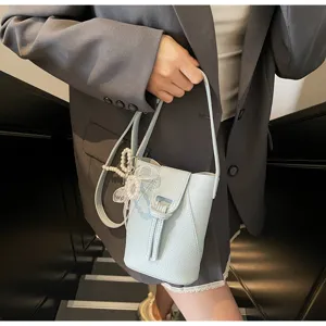 Light blue mini bucket phone bag with pearl bow charm, elegant crossbody detail view