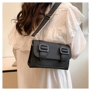 Detail view of the black leather crossbody satchel bag, featuring dual buckles and wide strap.