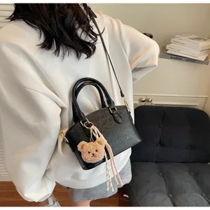 Vue détaillée du sac à main pour femme noir motif croco avec joli pendentif en peluche.