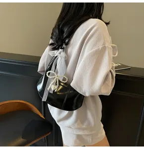 Detail view of stylish black glossy dumpling shoulder bag with elegant pearl bow decoration.