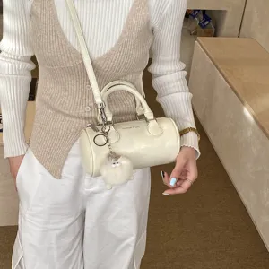 Small white cylinder handbag for women, PU leather crossbody pillow bag with cute plush pendant.