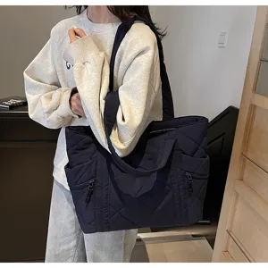 Detail shot of a stylish dark blue quilted tote bag with side zipper pockets and shoulder strap.