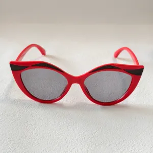 Nahaufnahme von roten Kinder-Cat-Eye-Sonnenbrillen mit Glitzer-Brauenlinie und Graugläsern.