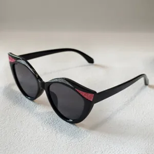 Kinder Katzenauge Sonnenbrille mit Glitzer Details, stilvoller schwarzer Rahmen und dunklen Gläsern.