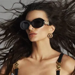 Primer plano detalle de gafas de sol ovaladas oversize de lujo con acentos dorados icónicos.