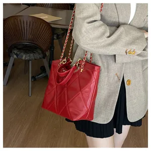 Red quilted tote bag featuring gold chain straps and chic texture, elegant detail view.