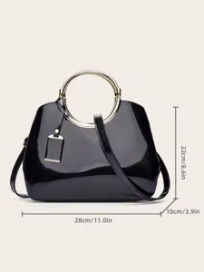 Detalle del bolso de mano de charol negro con acabado brillante y elegante asa redonda de metal dorado.