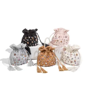 Rhinestone embellished drawstring bucket bag with pearl handle and tassels, elegant design.