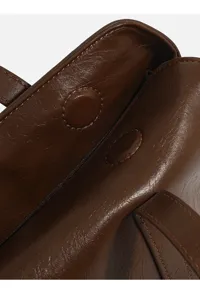 Close-up detail of dark brown women handbag magnetic snap closure and leather texture.