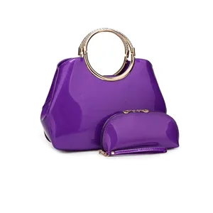 Detalles del bolso de charol violeta, acabado brillante y asa redonda de metal dorado.