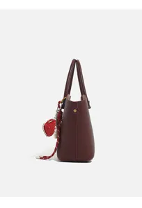 Side detail view of burgundy pebbled leather women handbag with charming red pendant detail.