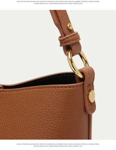 Detailed view of brown leather bucket bag featuring gold tone metal ring and adjustable strap.