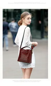Close-up view of the glossy dark red crocodile pattern bucket bag worn by model outdoors.