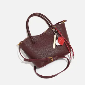 Stylish burgundy women's handbag with top handle and crossbody strap, baseball charm.