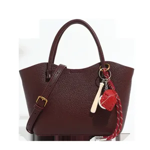 Burgundy leather tote bag with crossbody strap and baseball charm for women daily commute.