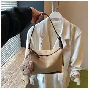 Detail view of the brown suede underarm shoulder bag featuring a cute plush dog charm and zipper.