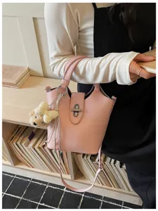 Detail view of a stylish pink leather bucket bag with cute bear keychain in a cozy lifestyle setting.