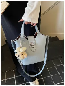 Stylish light blue leather bucket bag with lock closure and cute plush bear charm detail.