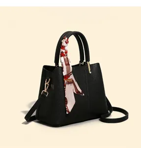 Detailed view of black leather handbag featuring gold tone hardware and chic printed silk scarf.