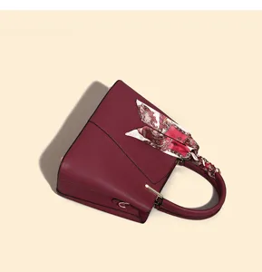 Red leather handbag detail close-up showing textured finish and decorative patterned scarf handle.