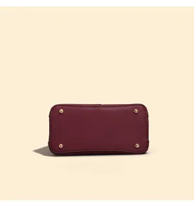 Burgundy handbag bottom detail with metal protective feet, showing durable quality design.