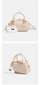 Vista dettagliata della borsa beige coccodrillo con applicazione a cuore e ciondolo soffice.