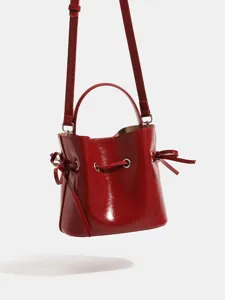 Red patent leather bucket bag with top handle and strap, perfect for summer wear.