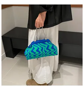 Detail shot of a blue and green wavy knit clutch bag with a chic metal chain handle.