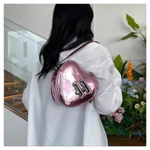 Sac bandoulière rose métallisé en forme de cœur porté par modèle, avec pendentifs.