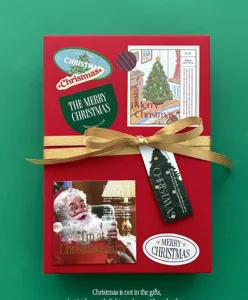 Christmas gift wrapping ribbon detail, red box with gold bow and festive decorative stickers.
