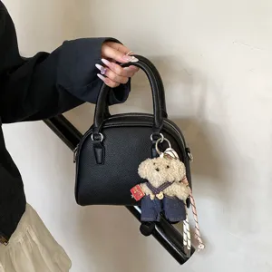 Korean style black litchi grain shell handbag with cute teddy bear pendant for women daily use.