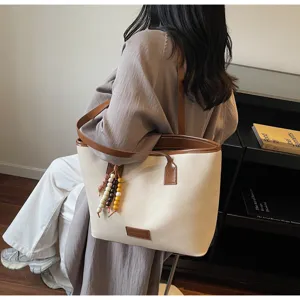 Detail view of large beige canvas tote bag with brown leather trim and bead charm.