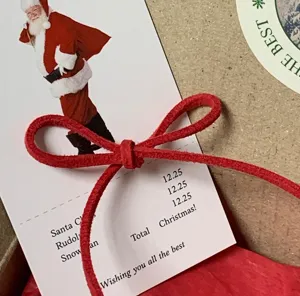 Primo piano dettagliato di cordoncino in ecopelle rossa legato a fiocco su carta natalizia.