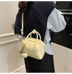 Close-up of a stylish light yellow retro bowling handbag with heart pendant and shoulder strap.