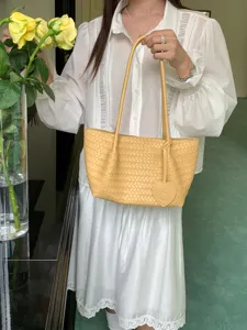 Cream yellow woven leather shoulder tote bag with heart charm, stylish casual design.