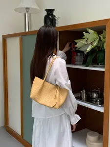 Woven shoulder bag detail, pastel yellow tote with cute heart pendant, casual resort style.