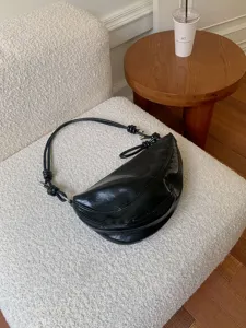 Detail view of a stylish black glossy shoulder bag with knotted strap on white chair.