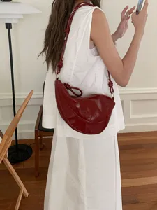 Stylish women's dark red patent leather crescent shoulder bag featuring a unique knotted strap.