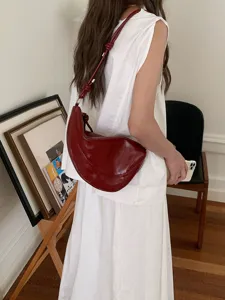 Dark red patent leather hobo shoulder bag with stylish knotted strap, chic minimalist design.