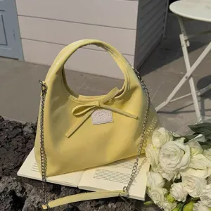 Detailed view of stylish yellow crossbody bag with bow and chain strap in outdoor setting.