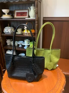 Detailed view of woven leather shoulder tote bags in black and green with heart charms.