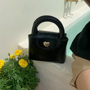Chic black structured handbag with gold heart lock and rounded handle, perfect lifestyle detail.