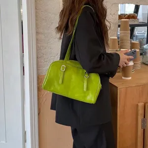Detail view of a stylish green underarm shoulder bag with belt buckles in a chic cafe setting.