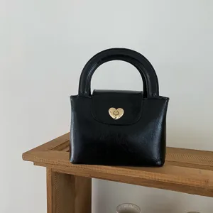 Detailed view of black leather handbag featuring a golden heart lock and chic rounded handle.