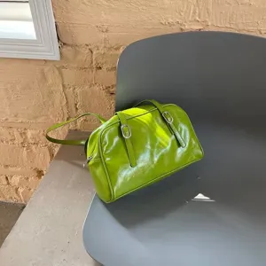 Close-up detail of the green glossy leather shoulder bag, highlighting retro buckle straps.