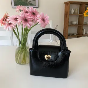 Detail shot of black textured handbag with golden heart lock and chic top handle on white table.