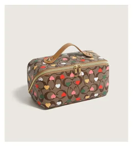 Detailed view of brown printed cosmetic bag with heart pattern, handle and double zipper closure.